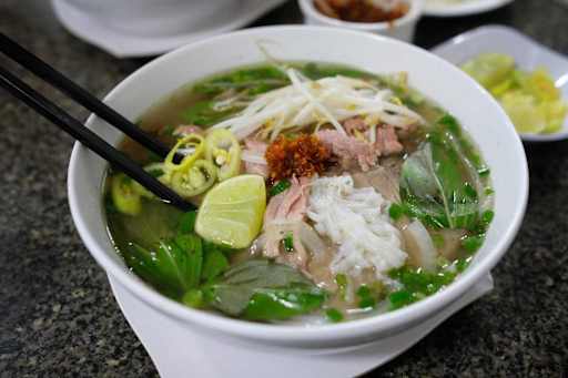 Phở bò, Vietnamese beef noodle soup, with rice noodles, beef, bean sprouts, basil, green chilies, green onions, lime, chili paste, and chopsticks.