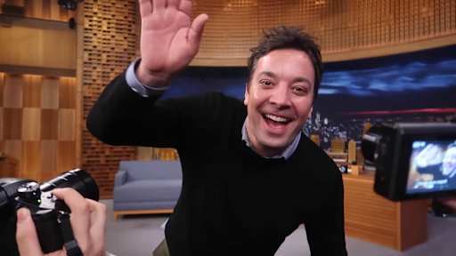 Jimmy Fallon smiles and waves on the set of *The Tonight Show* in 2019.