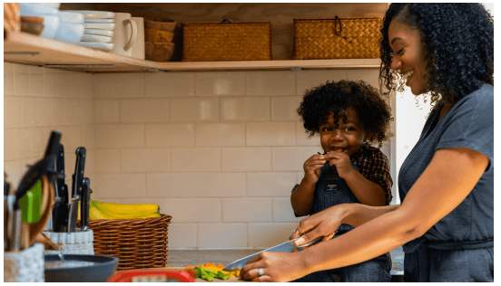 A mother and child smiling while preparing food together in a kitchen