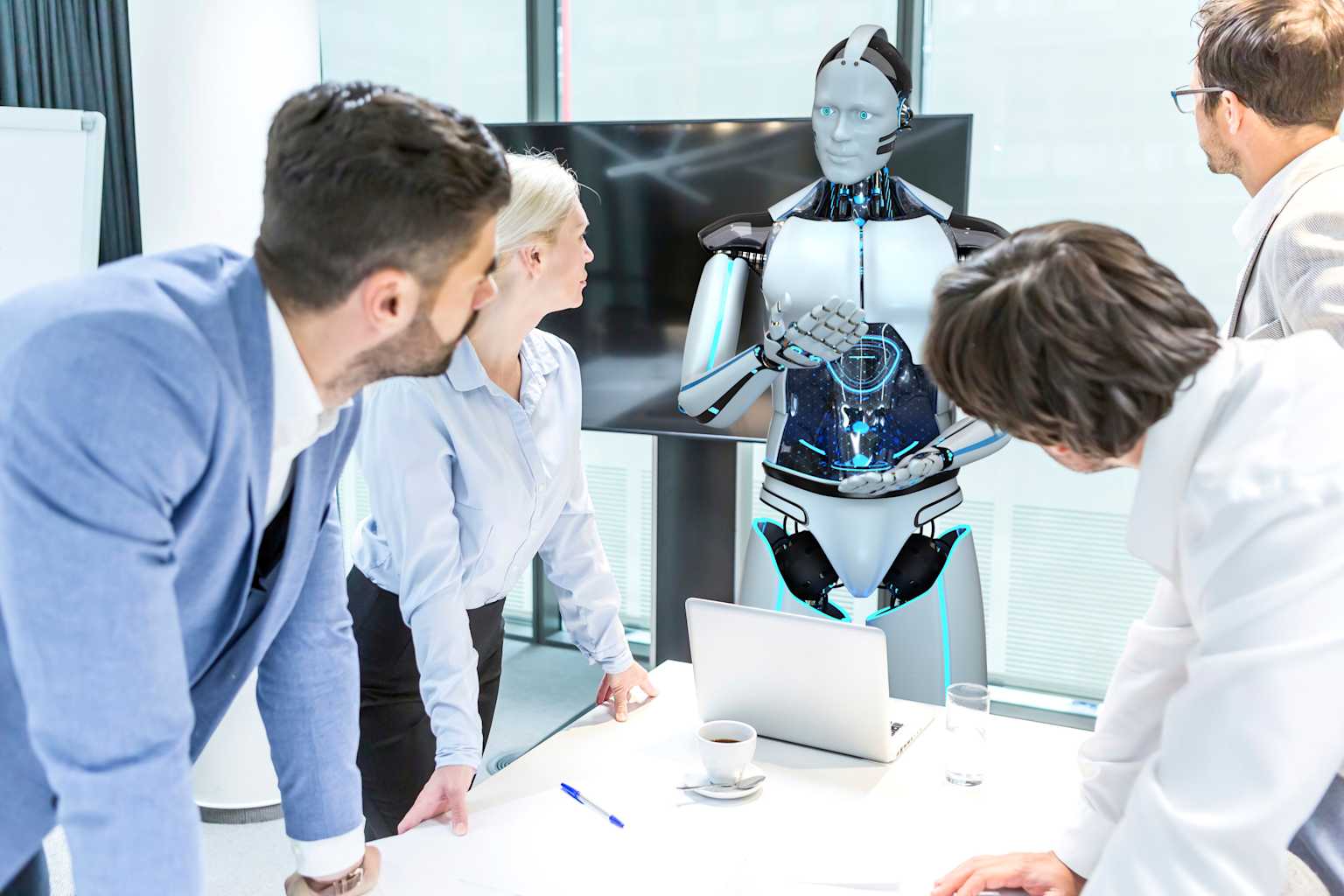 Humanoid robot collaborating with human professionals in a modern office meeting, illustrating AI-human hybrid staffing solutions.