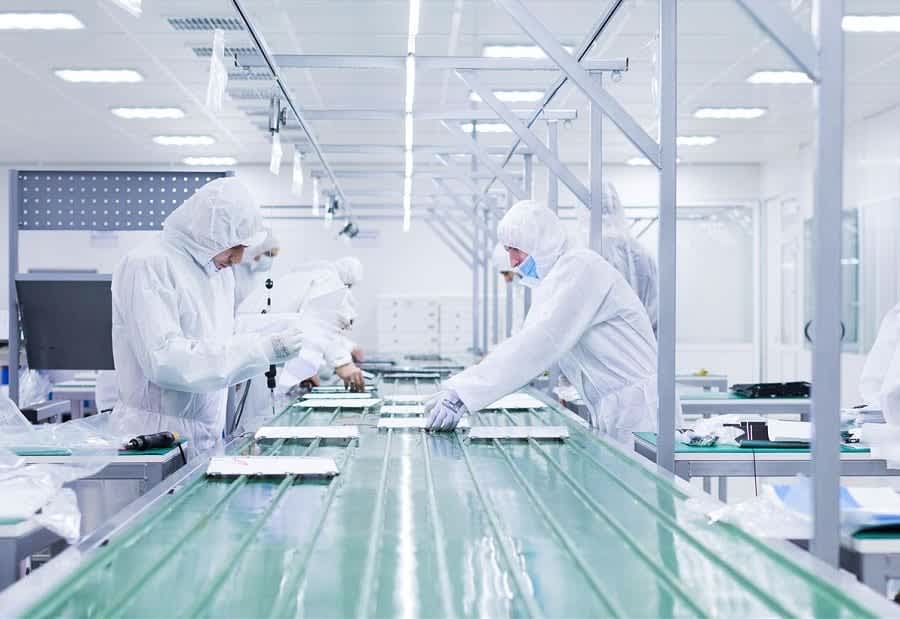 Workers in cleanroom attire assemble components on a conveyor belt in a flat display manufacturing facility