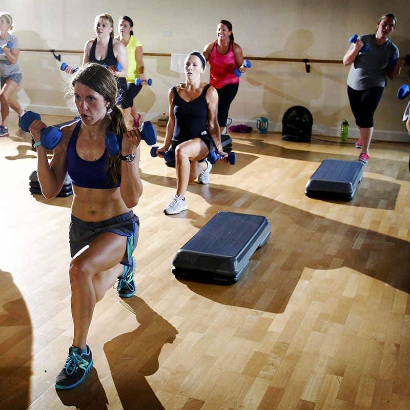 Women participating in a high-intensity interval training workout with dumbbells and steps.