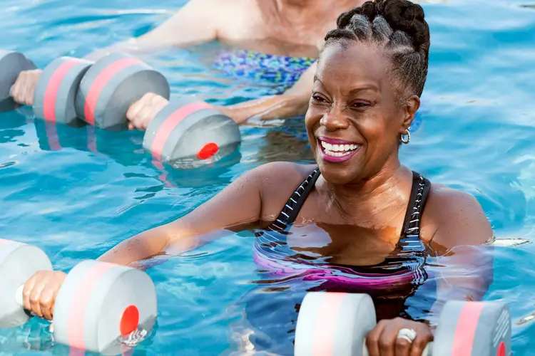 A woman doing water aerobics with buoyant dumbbells in a pool.