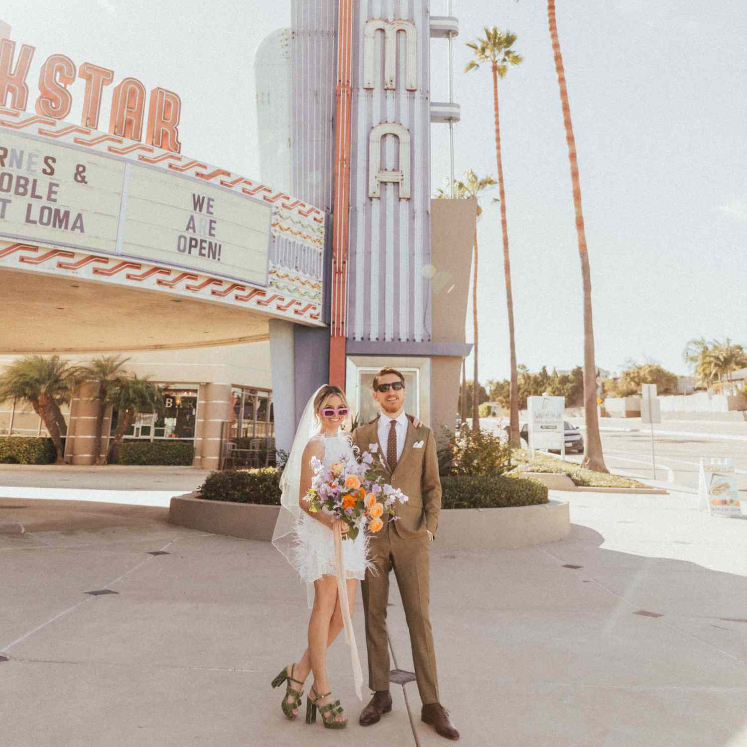 A bride and groom pose outside a vintage movie theater on their wedding day