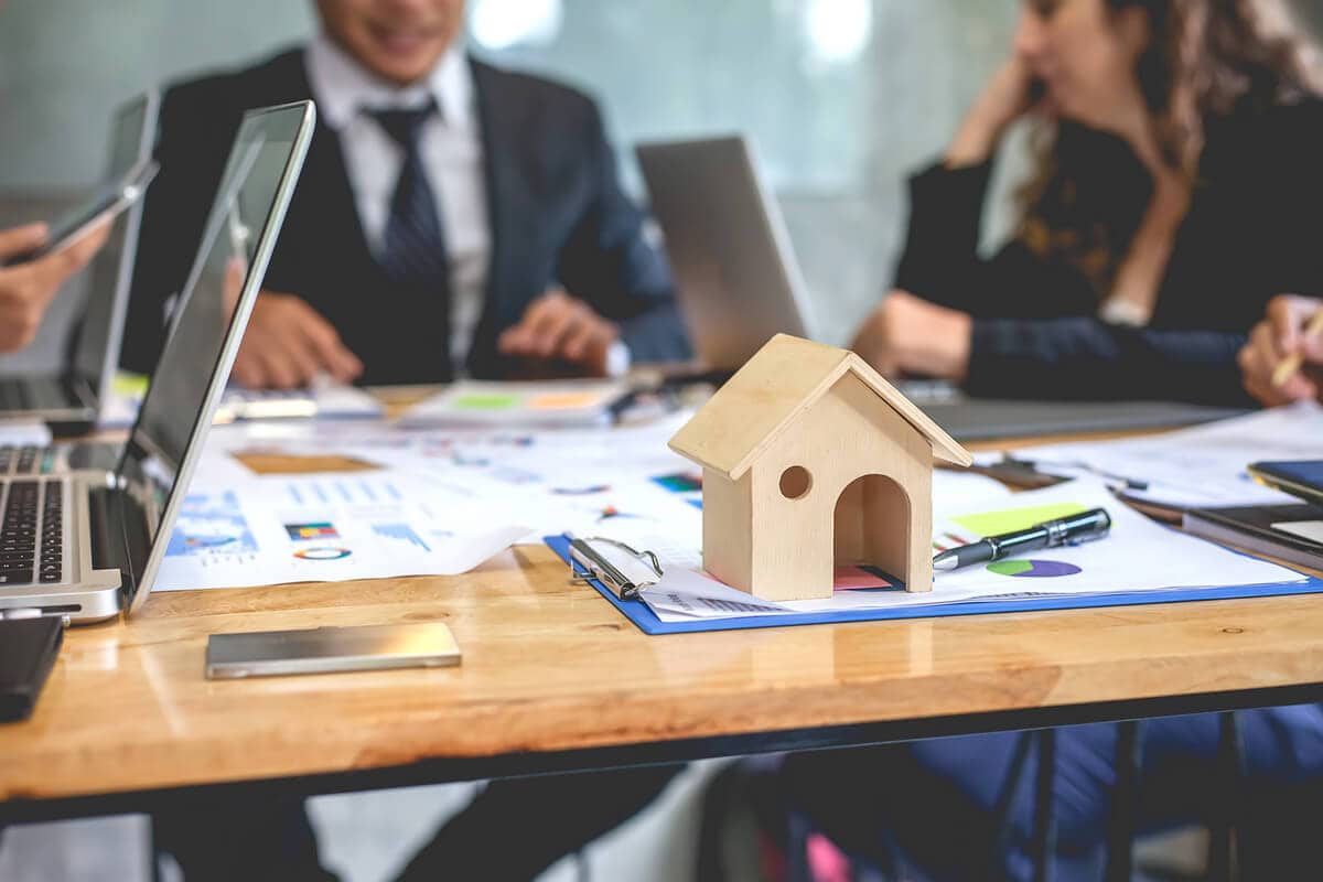 Professionals discuss real estate transactions in a meeting setting, with a miniature house model symbolizing property