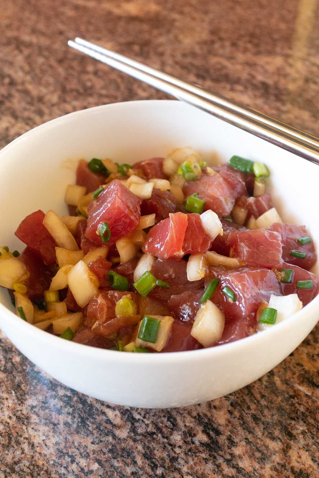 Fresh Hawaiian poke bowl made with cubed raw tuna, green onions, and onions served in a white bowl with chopsticks