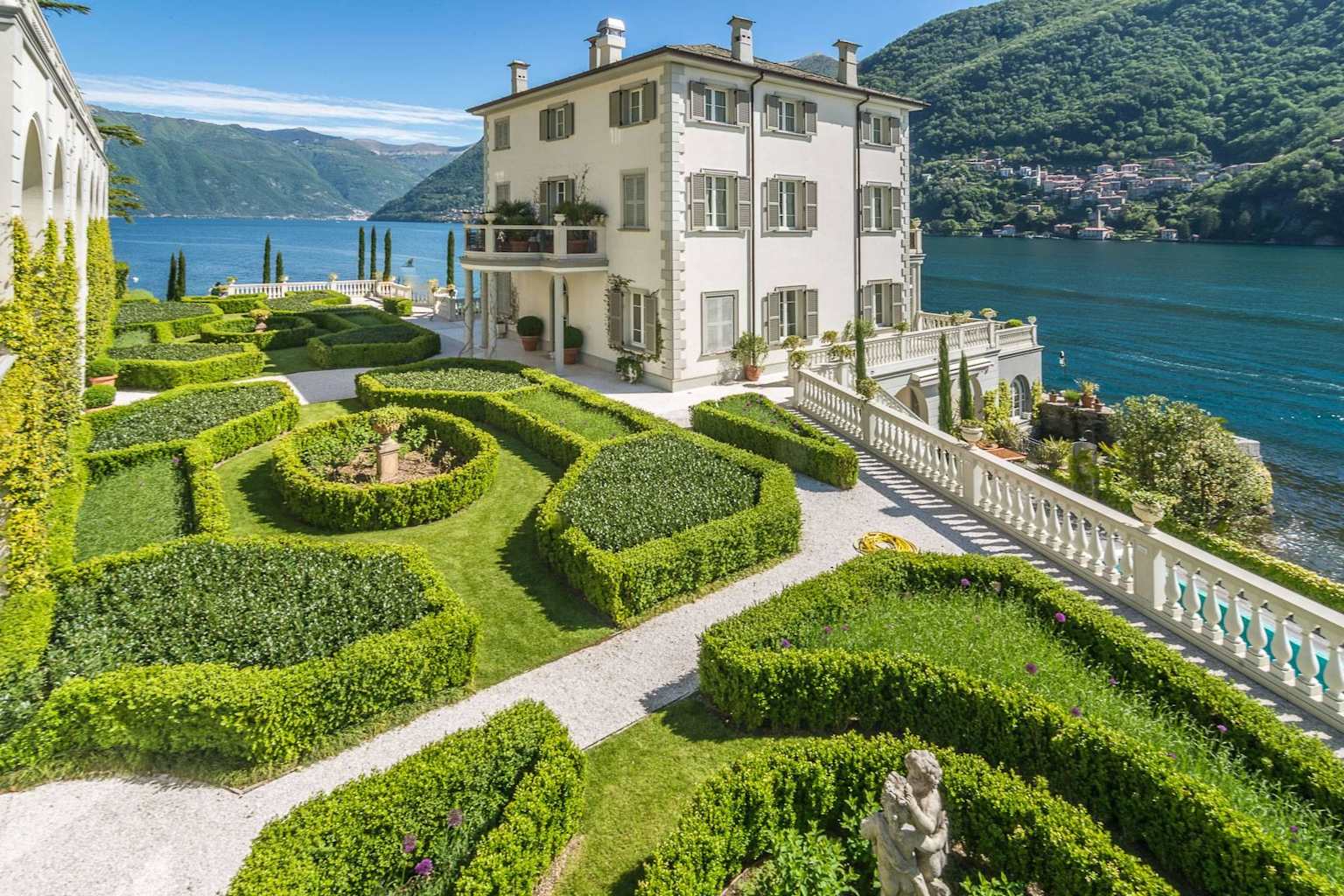 A grand white villa with sculpted gardens overlooks Lake Como, showcasing an exclusive private estate