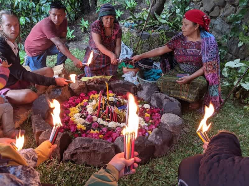 People gathered around a stone enclosure holding candles during a ceremony