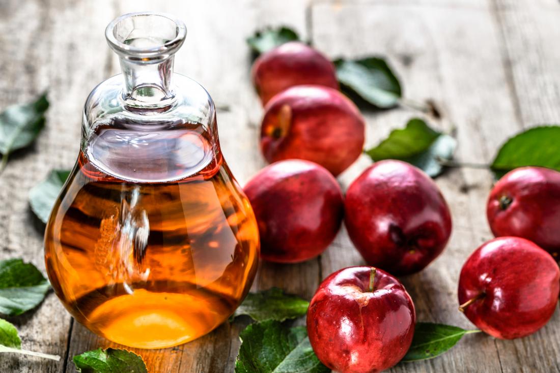 Apple cider vinegar in a glass bottle surrounded by fresh red apples