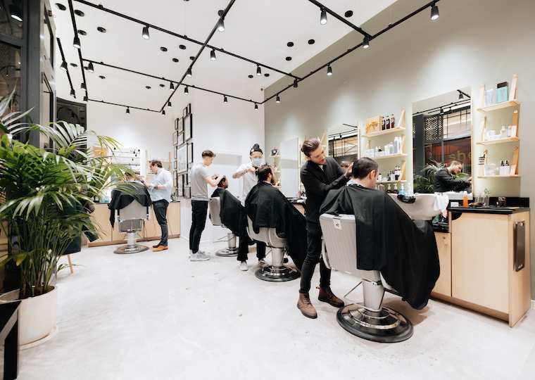 A clean, modern barbershop interior with several barbers attending to clients.