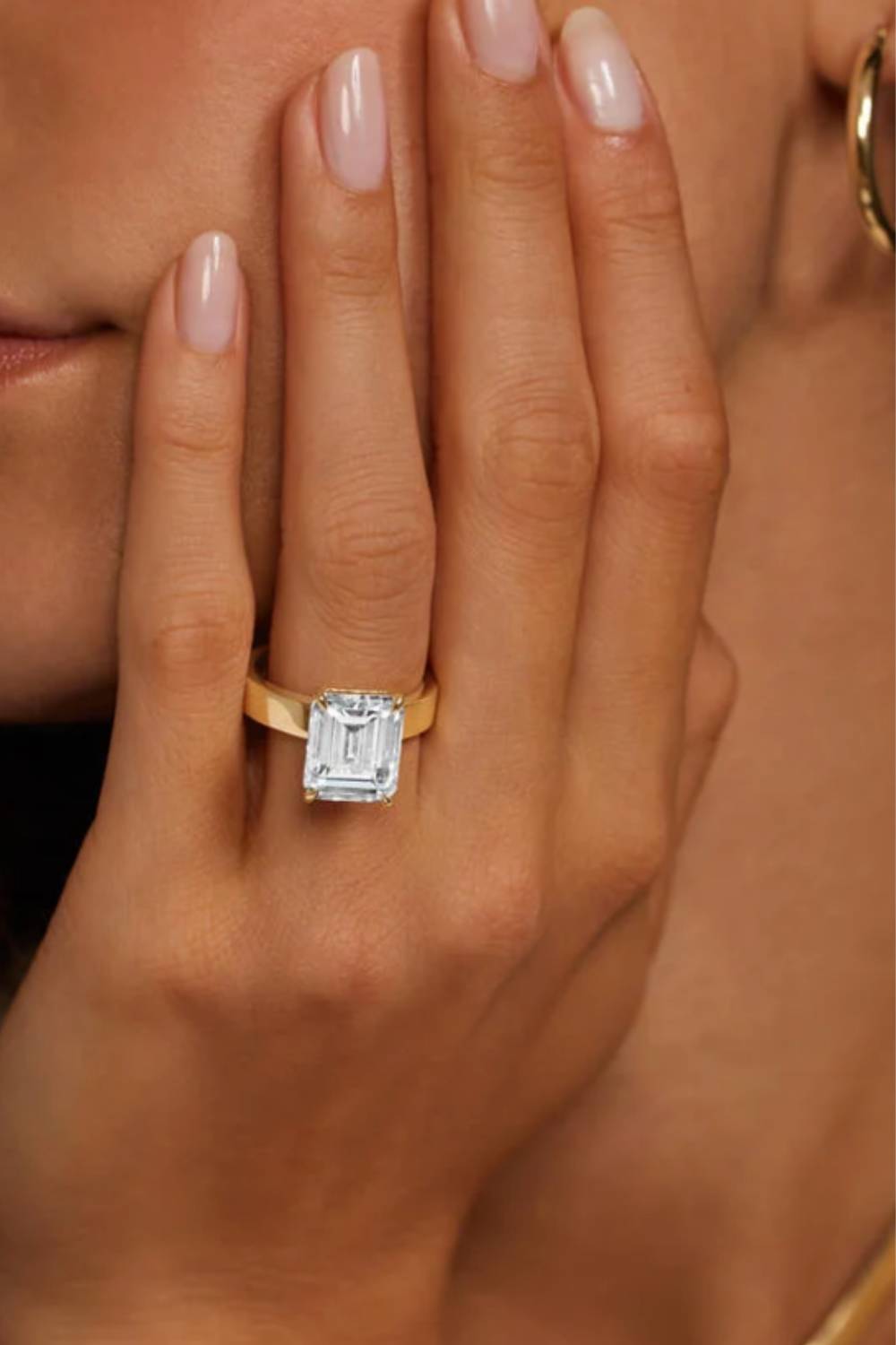 A modern solitaire engagement ring features a large emerald-cut diamond set in a yellow gold band