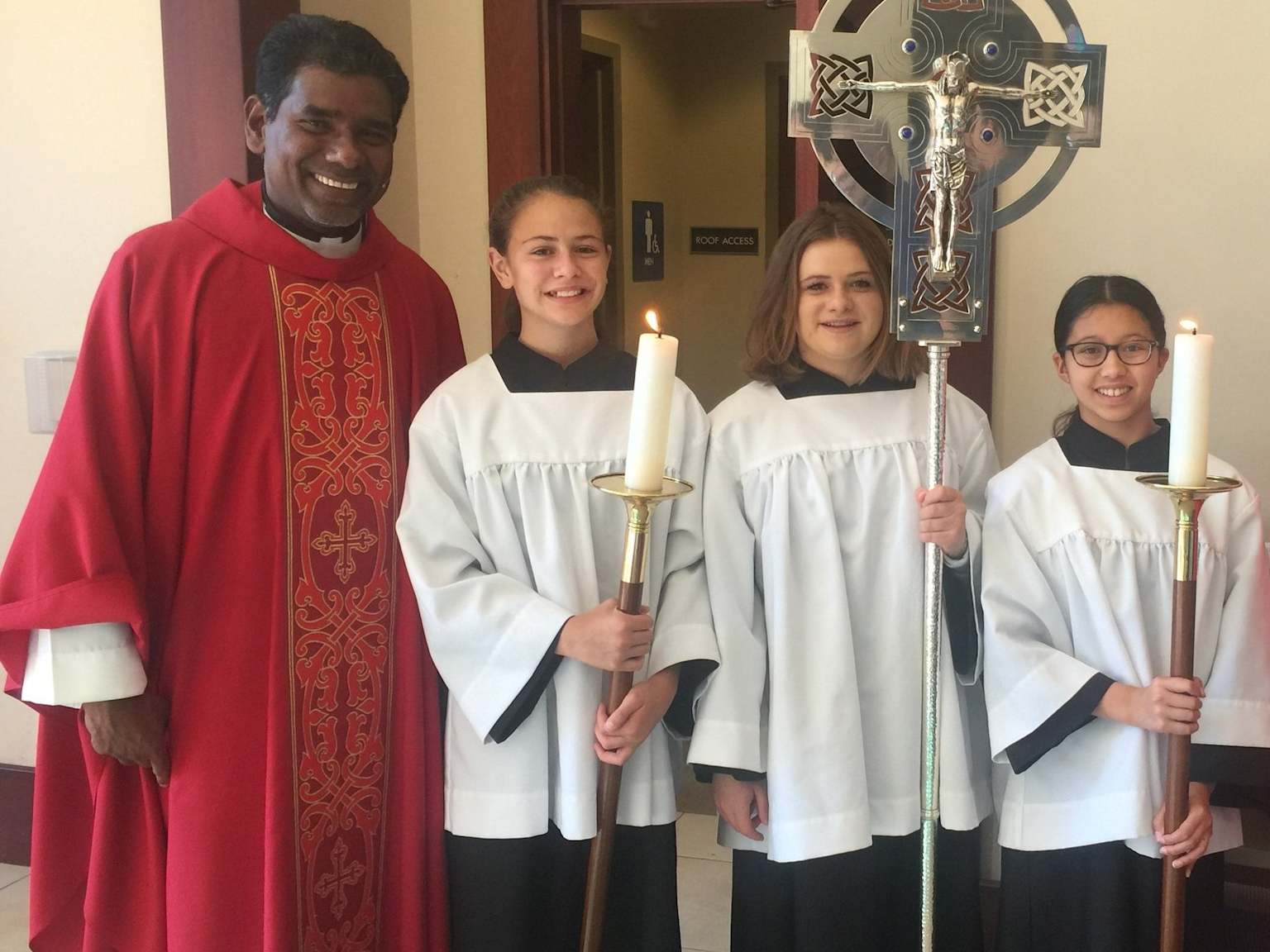 A priest and altar servers pose together inside a Catholic Church