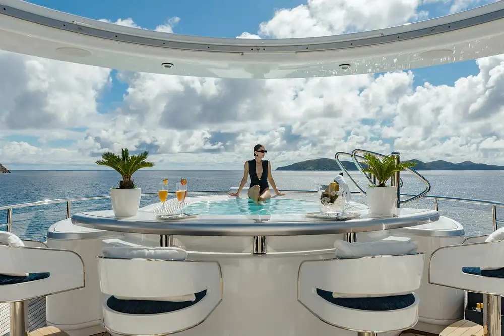 Woman relaxing in a jacuzzi on a luxury yacht deck with premium seating and drinks overlooking the ocean