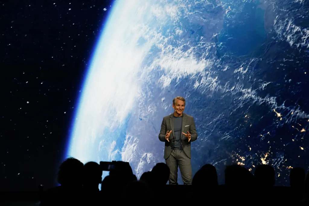 Presenter at a technology conference with a large Earth image backdrop, symbolizing innovation and AI breakthroughs.