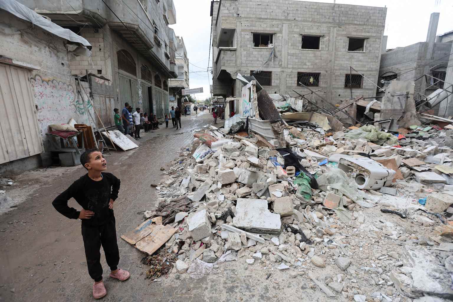 A boy stands on a rubble-filled street in a conflict-affected area, reflecting the human impact of Middle East tensions