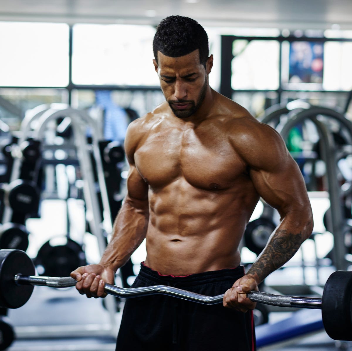 A muscular bodybuilder intensely works out with an EZ curl bar in a gym