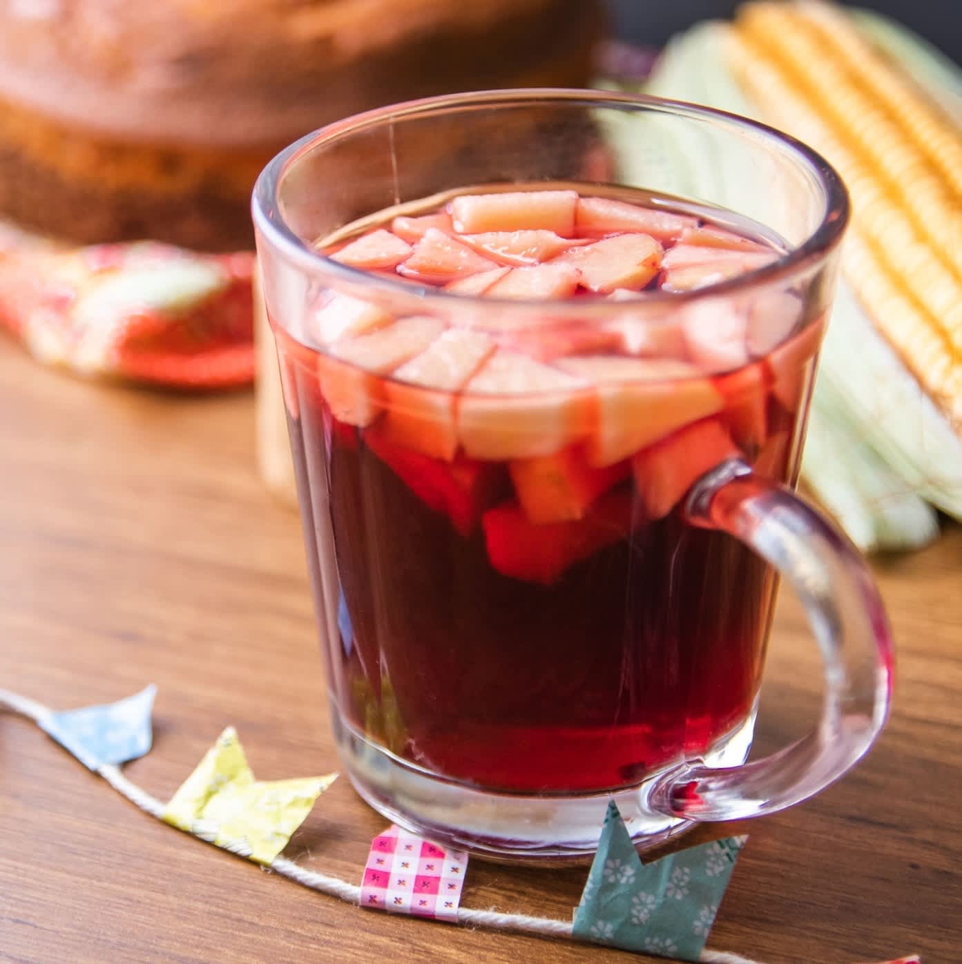 A glass of warm mulled wine or 'quentão' with fruit pieces, accompanied by Festa Junina decorations