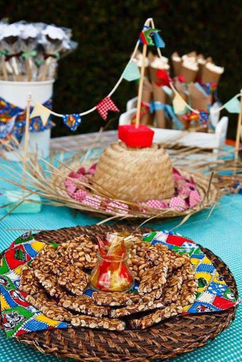 A festive Festa Junina table setting featuring pé de moleque, peanuts, straw decor, and colorful 'bandeirinhas'