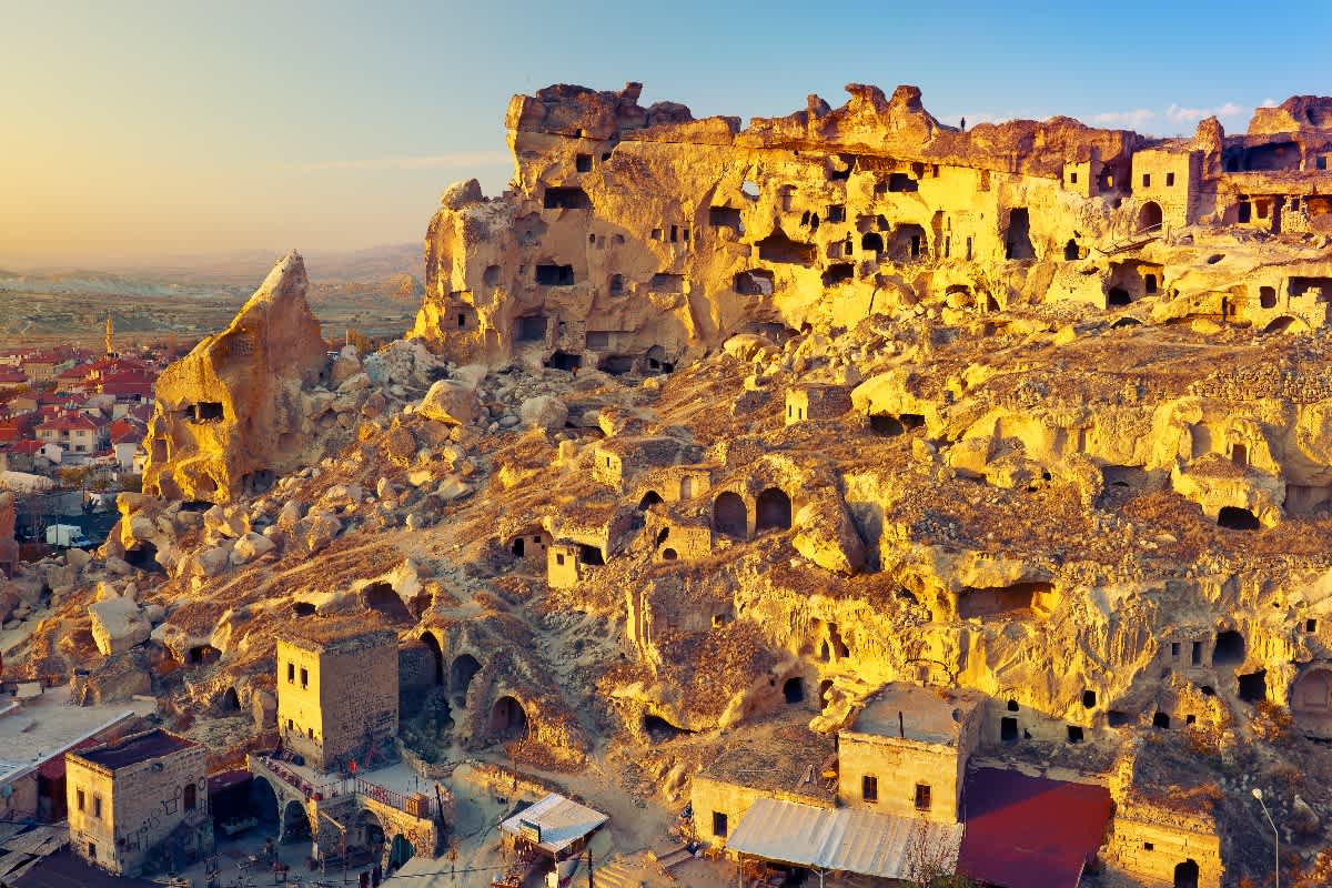 Sunlit rock formations and cave dwellings in Cappadocia, Türkiye, revealing entrances to historical underground settlements.