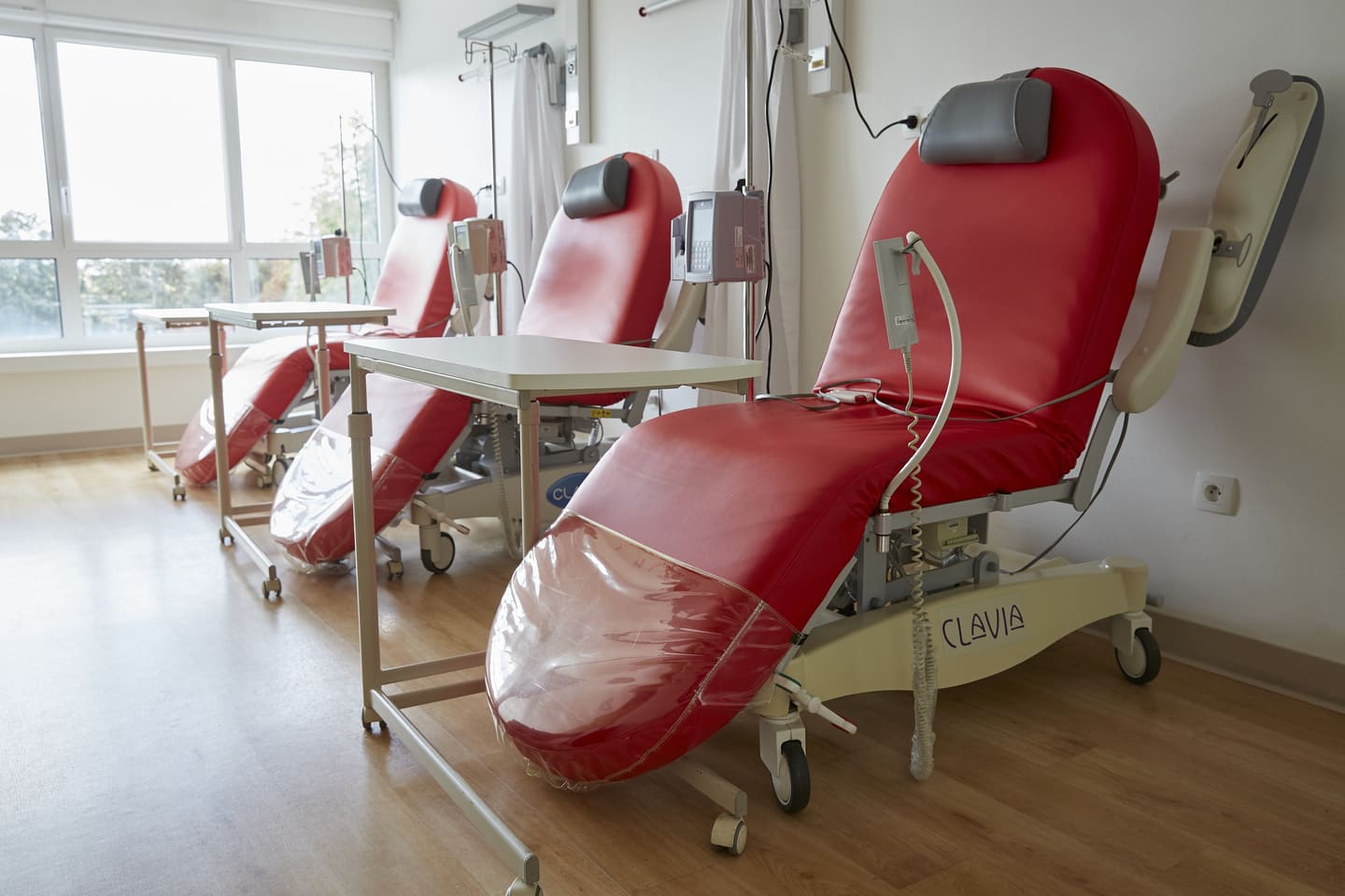 Modern red recliners in a bright, well-equipped outpatient chemotherapy treatment room