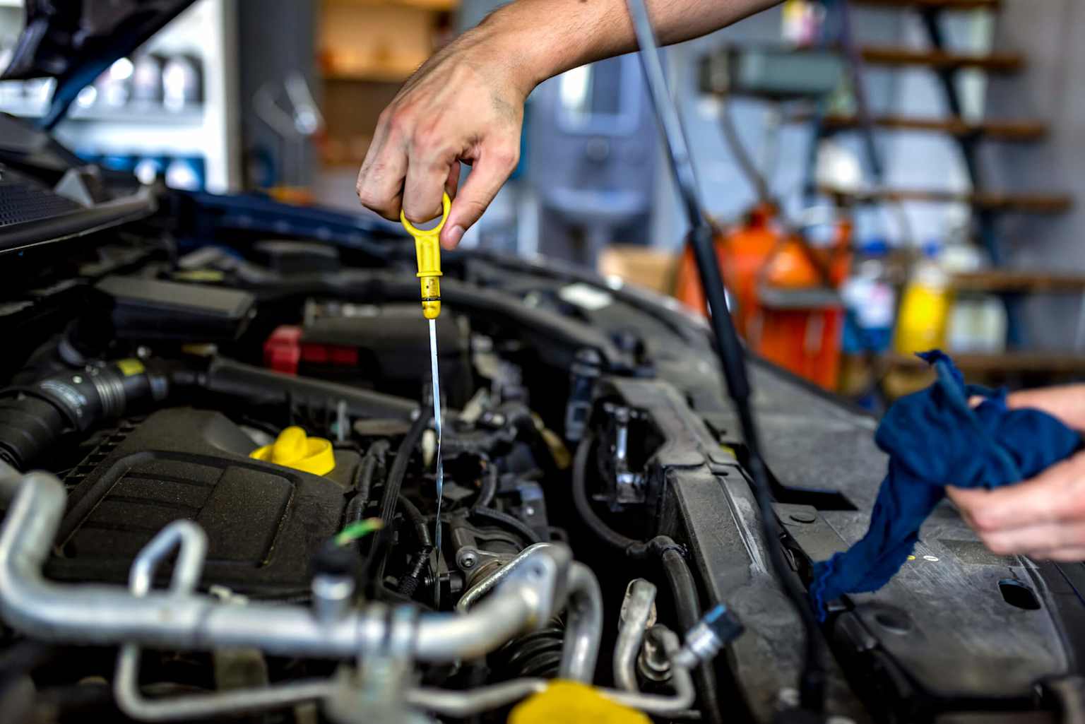 A person checking the engine oil level with a dipstick in a car's engine bay