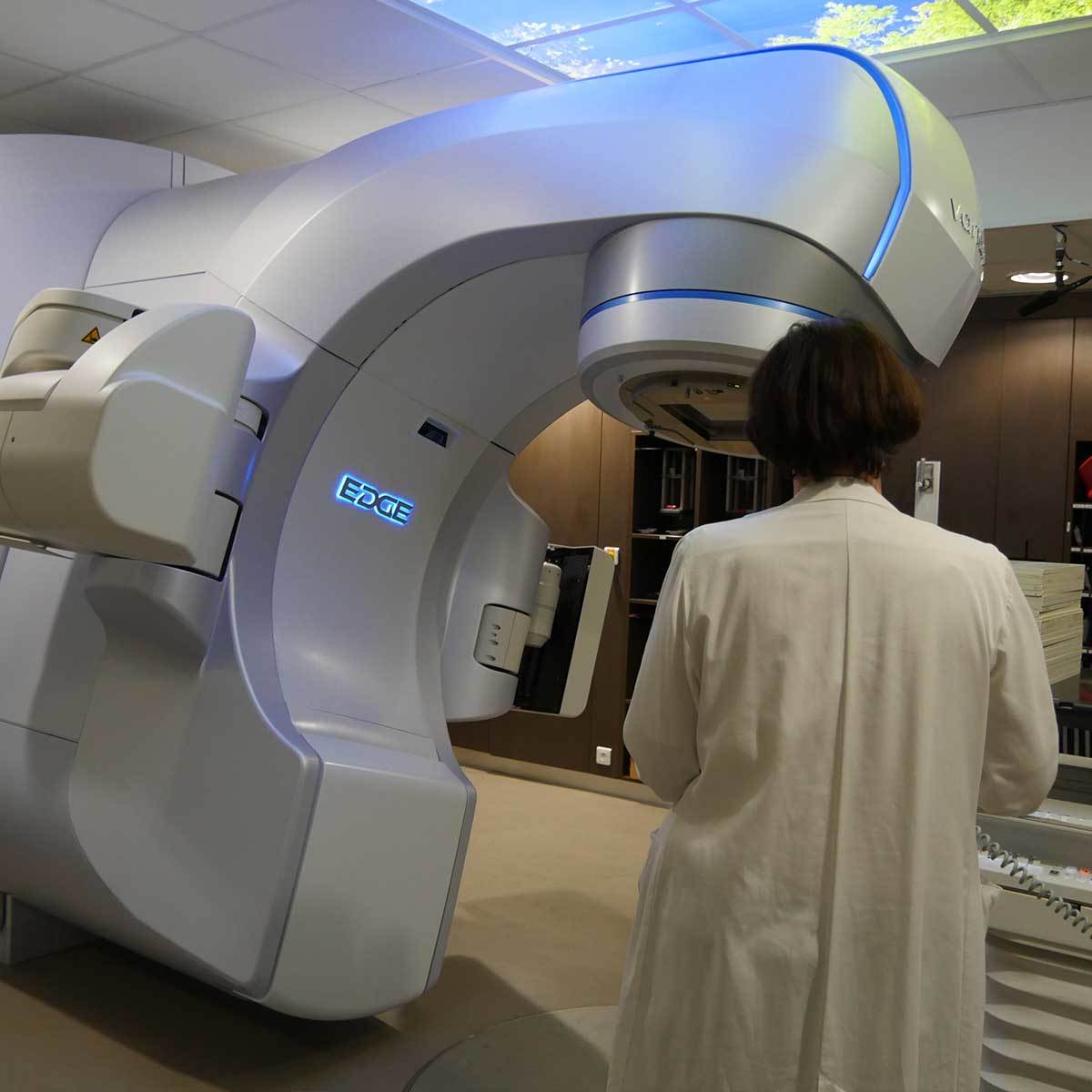 A modern EDGE linear accelerator, a key piece of equipment for radiotherapy, is shown with a medical professional observing