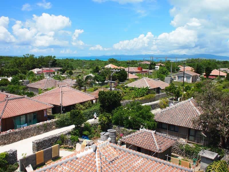 Panoramic view of Taketomi Island's traditional village, showcasing distinctive red-tiled roofs amidst lush greenery and the turquoise ocean