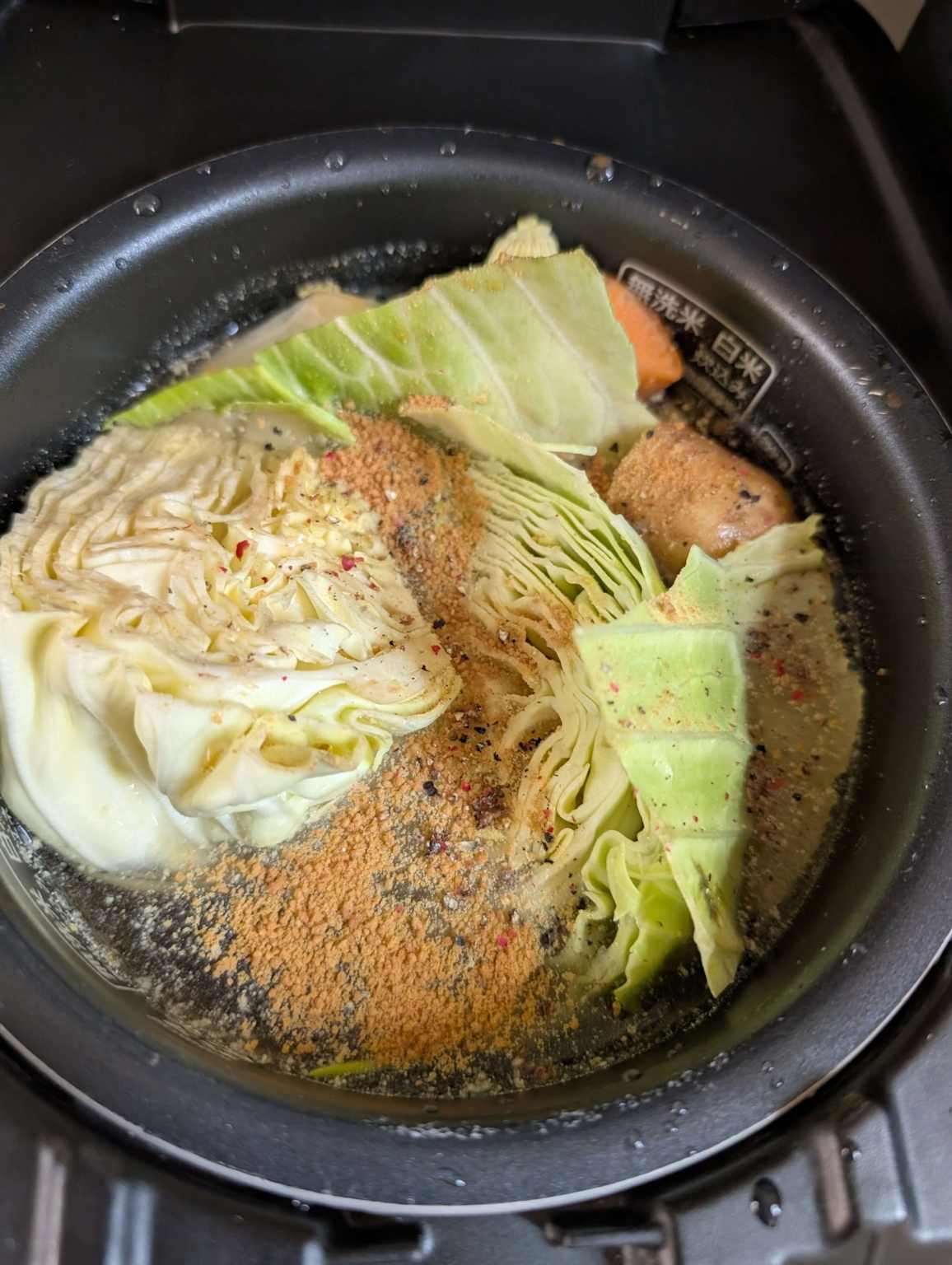 Ingredients including cabbage, carrots, and sausage cooking in a rice cooker with seasoning for a quick and easy meal