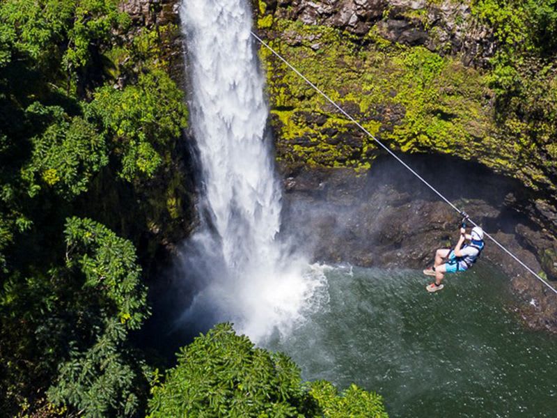 A person ziplines across a scenic waterfall and rainforest canopy in Hawaii, an adventure often cited as worth the extra cost