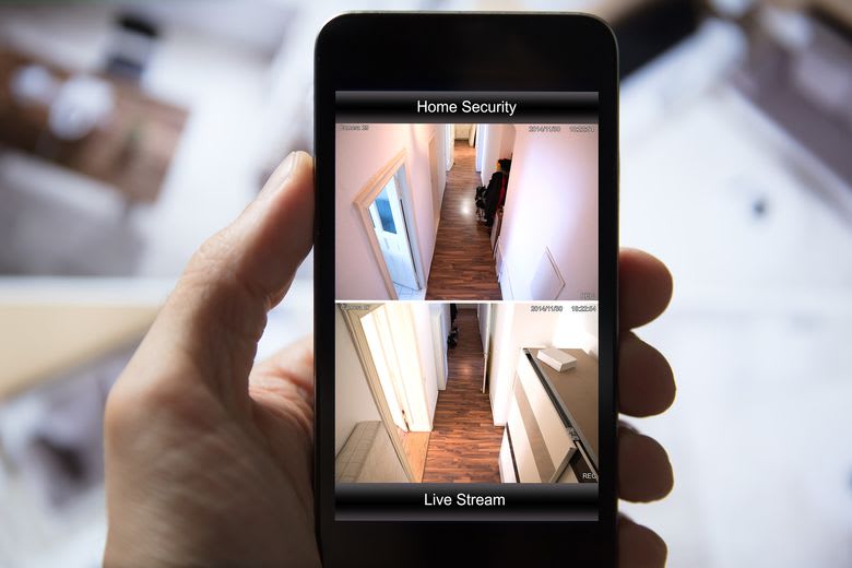 A smartphone displays a live stream from a home security system, allowing remote monitoring of the premises