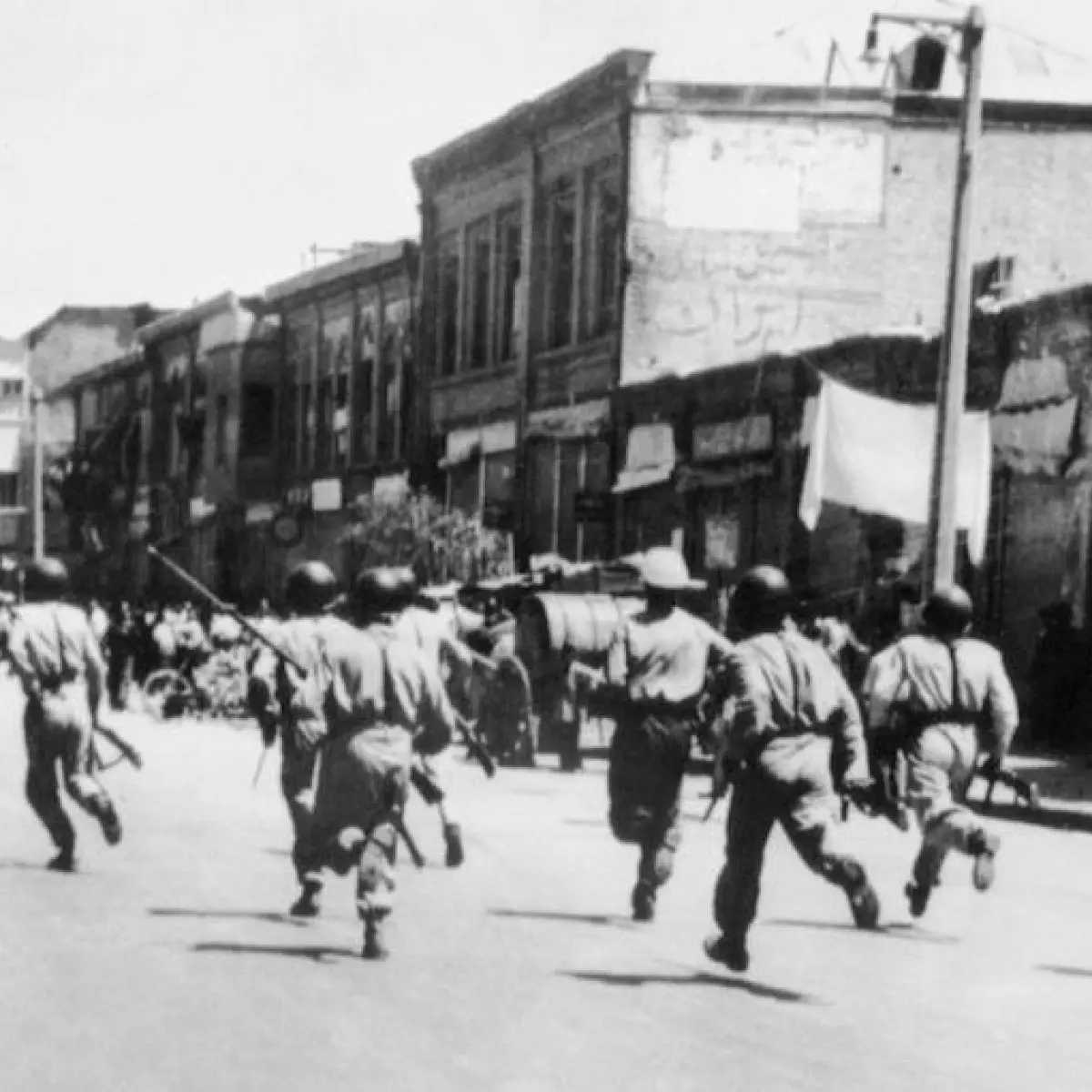 Uniformed individuals running through a street during the 1953 Iranian coup