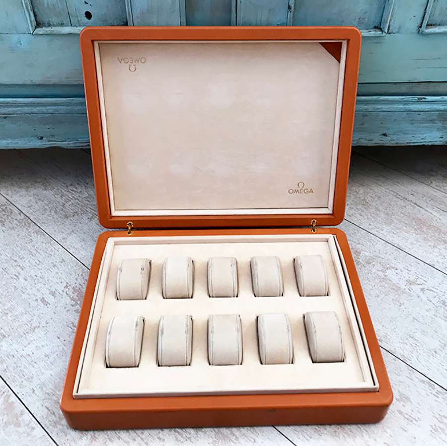 An open OMEGA professional watch box with ten empty cream-colored watch cushions