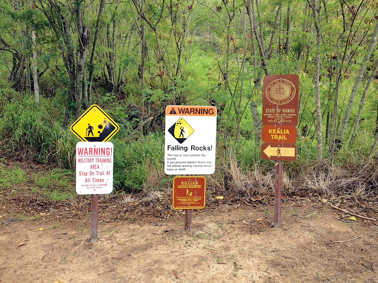 Warning signs on Hawaii's Kealia Trail caution hikers about military training areas and falling rock hazards to ensure safety