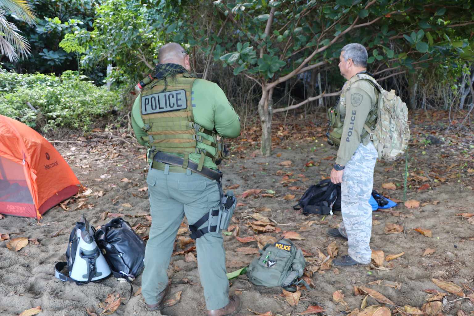 Law enforcement officers at an apparent illegal campsite in a Hawaiian natural area