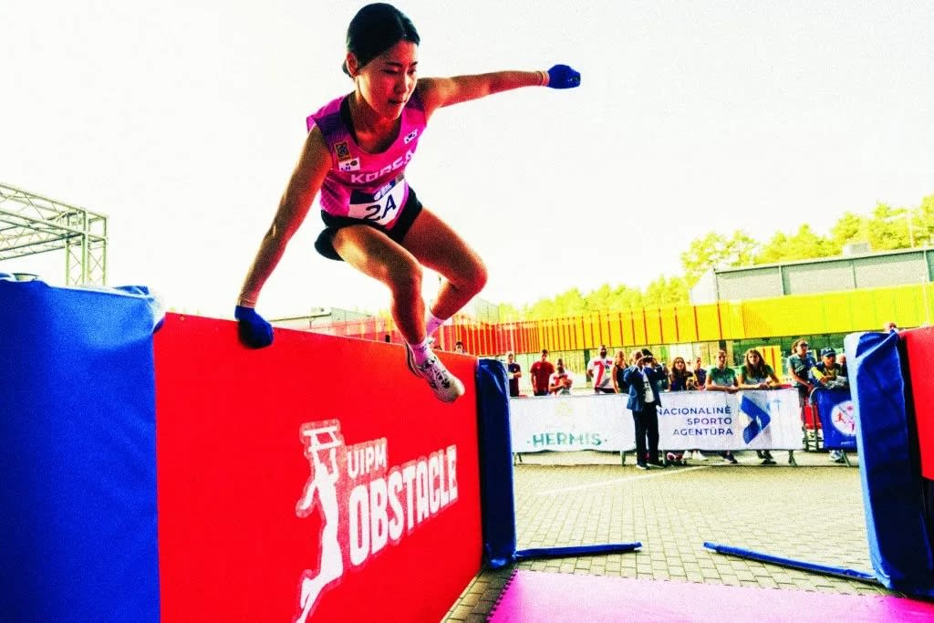 A Korean athlete navigates a red wall obstacle, part of the new UIPM Obstacle discipline in modern pentathlon