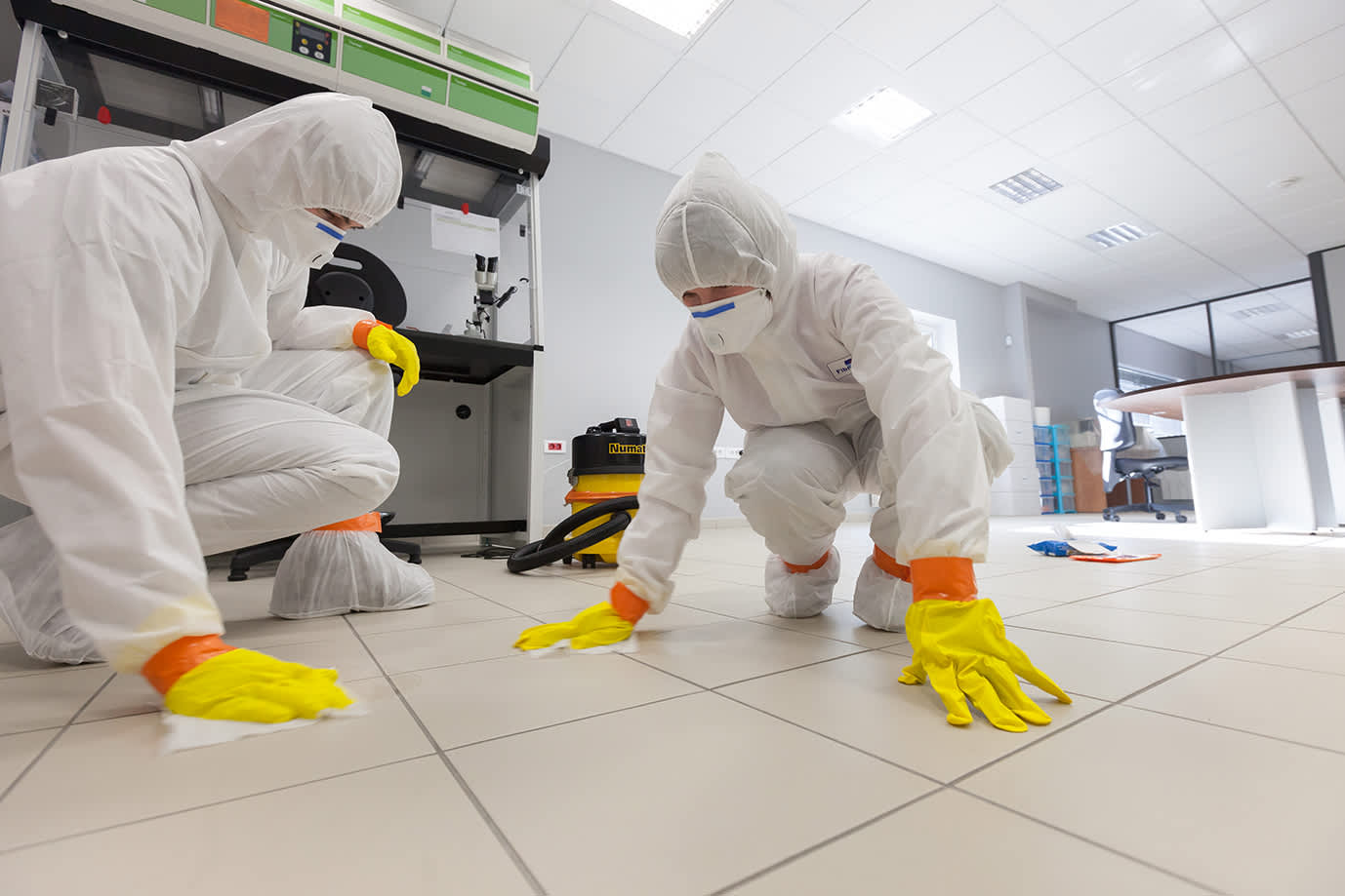 Specialized cleaning professionals in full personal protective equipment meticulously clean a tiled floor