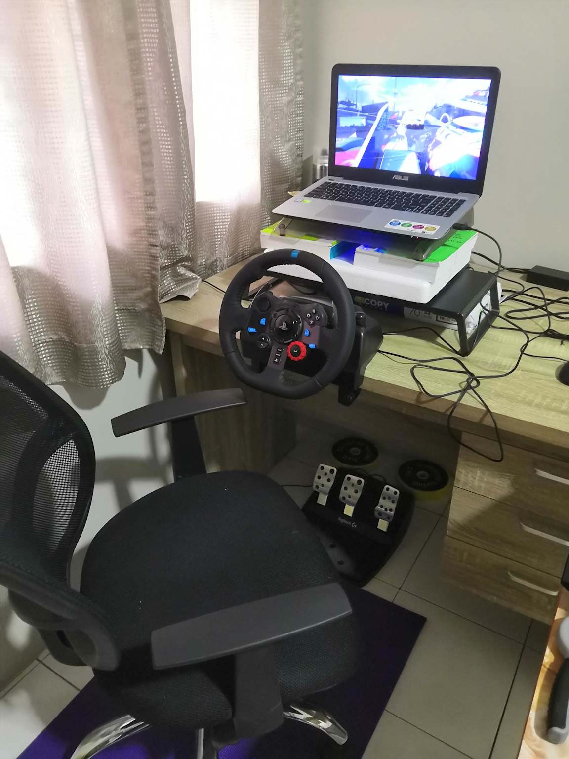A budget sim racing setup featuring a Logitech G29 racing wheel and pedals connected to a laptop