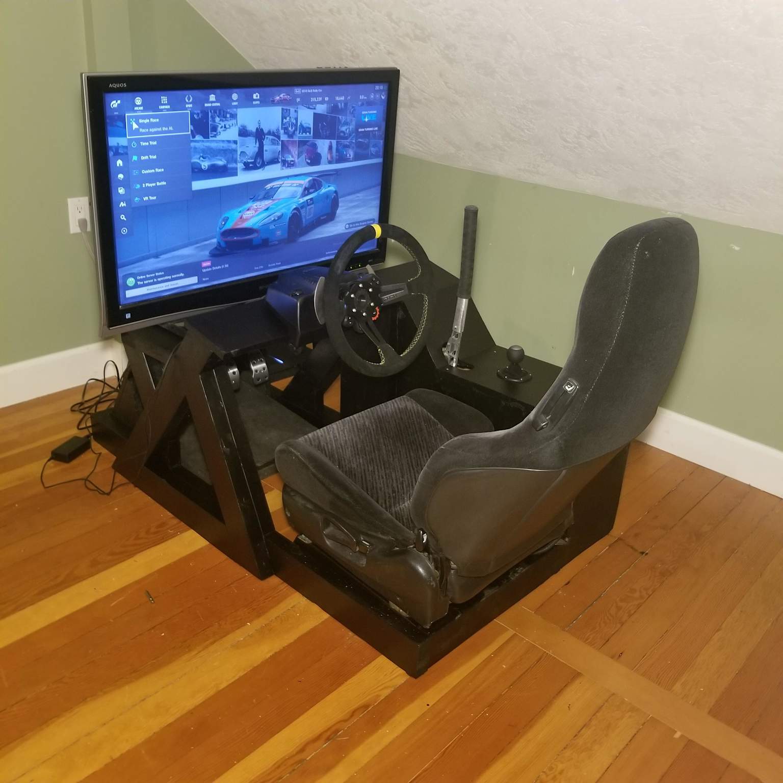A DIY budget sim racing rig featuring a Logitech G29 wheel, integrated car seat, and large monitor displaying a racing game