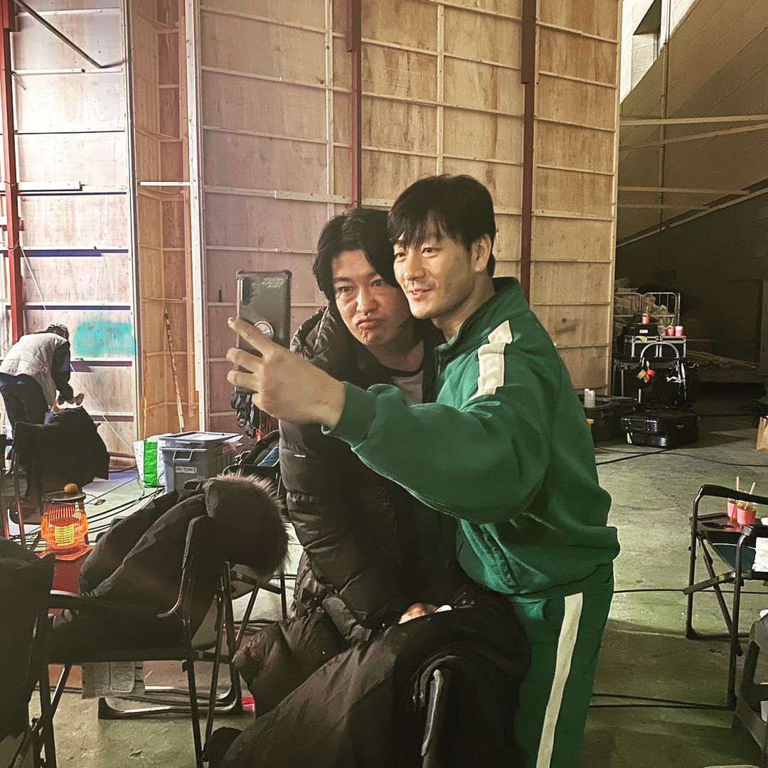 Actors from 'Squid Game' take a selfie on set, with one wearing the iconic green tracksuit.
