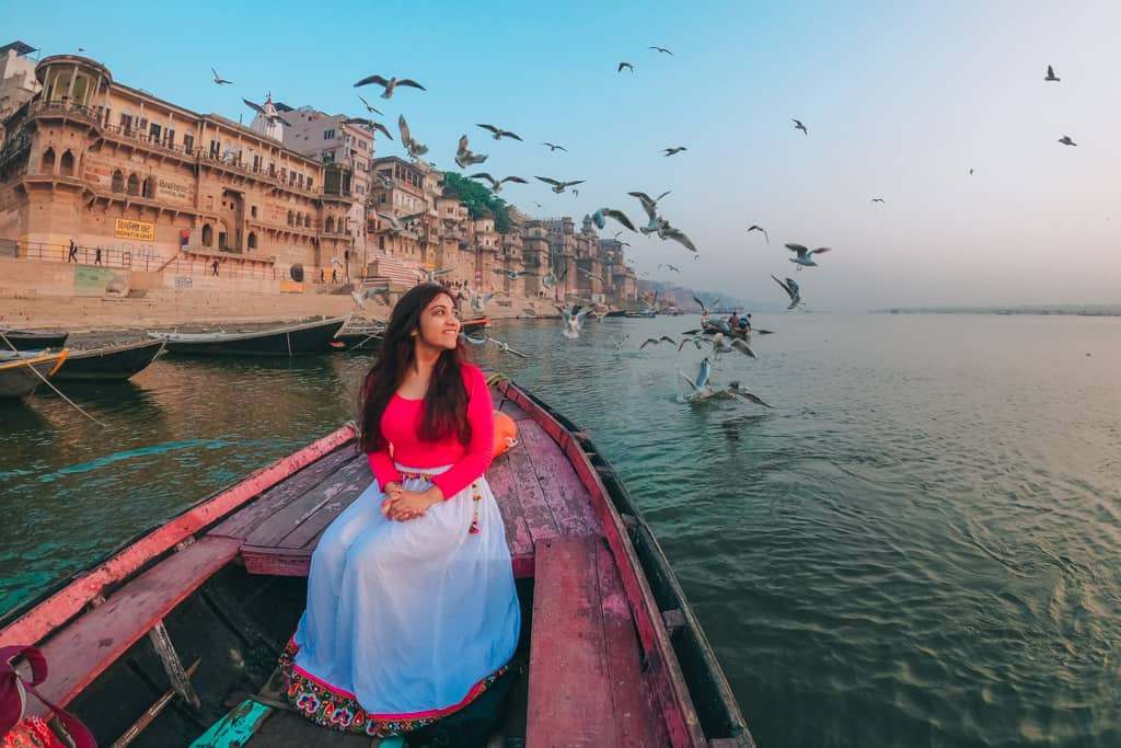 Woman enjoying peaceful boat ride on Ganges with flying birds at Varanasi ghats