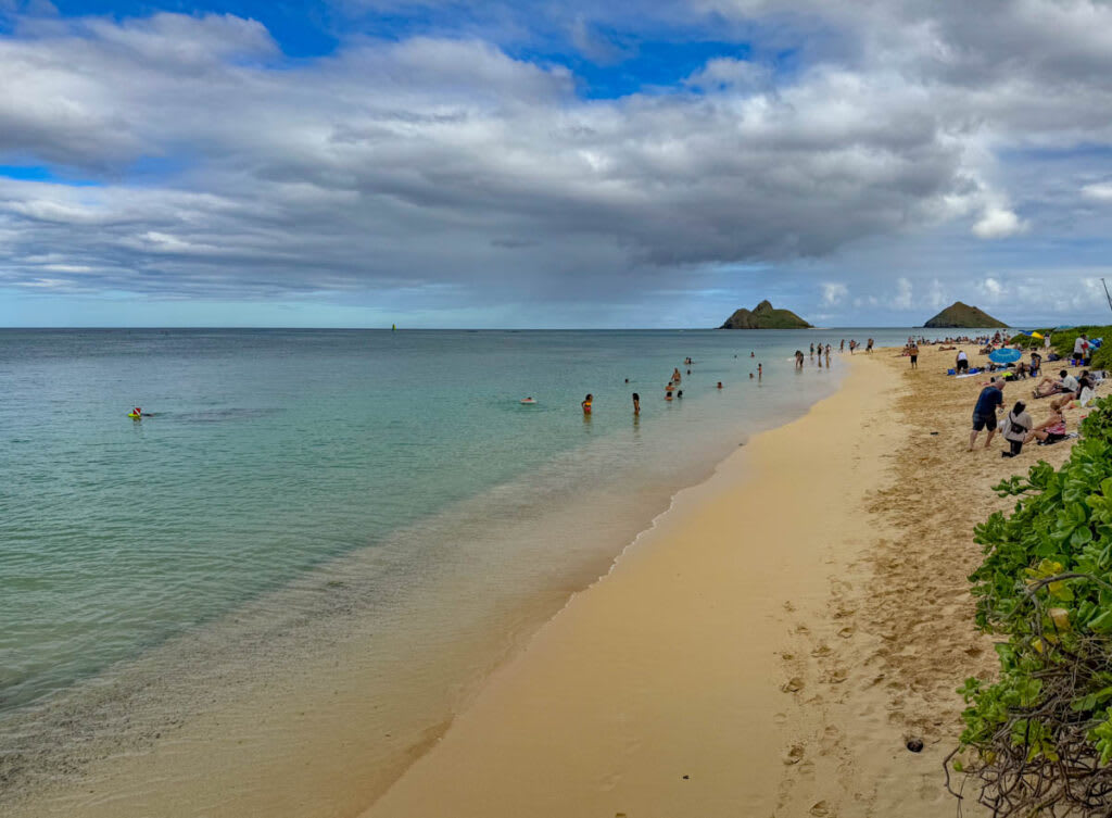 Swimmers and sunbathers enjoy the pristine waters and golden sands of Lanikai Beach, with the Mokulua Islands in the distance