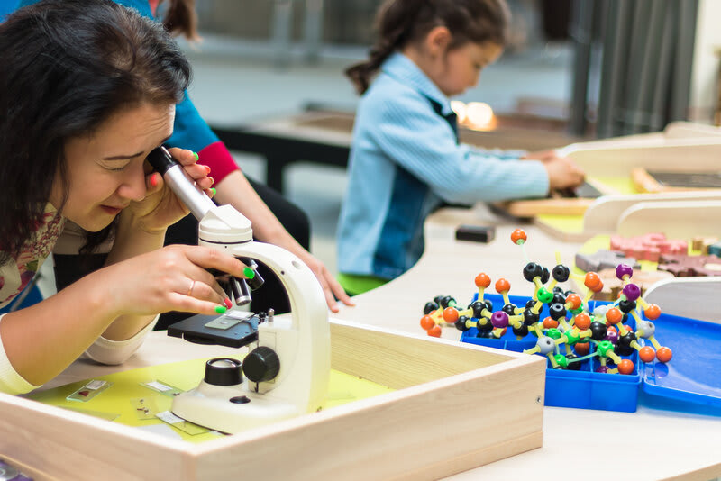 An adult and child engage in hands-on scientific exploration with a microscope and molecular models, highlighting experiential learning for future skills.