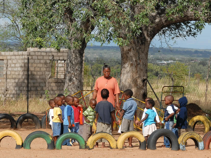 Young children engage in a community-based learning environment under the guidance of an adult in an African village