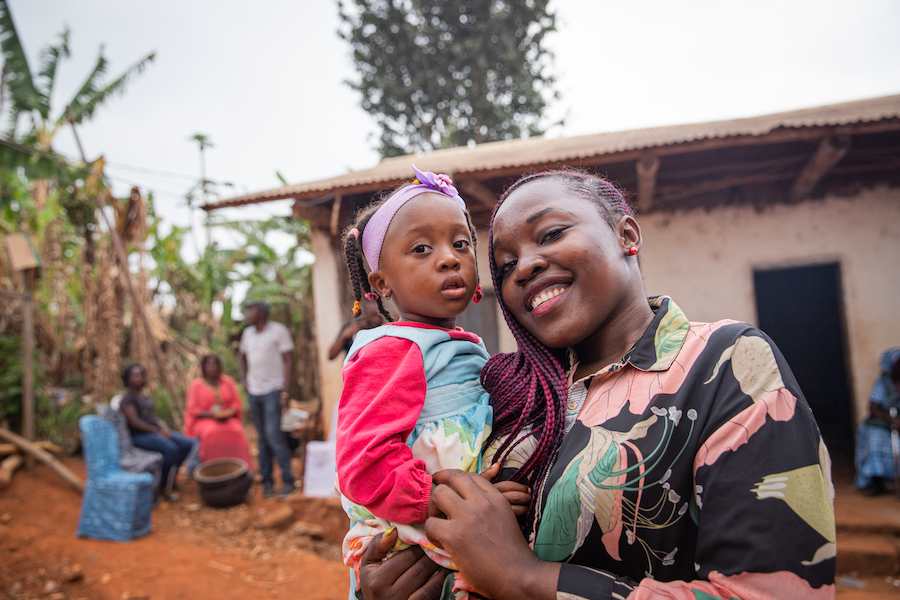 A woman holding a child in an African village, illustrating the community's role in traditional upbringing and education
