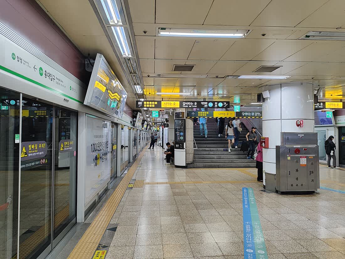 Interior view of Hongdae Station on Seoul Subway Line 2 showing platform screen doors, signage, and passengers.