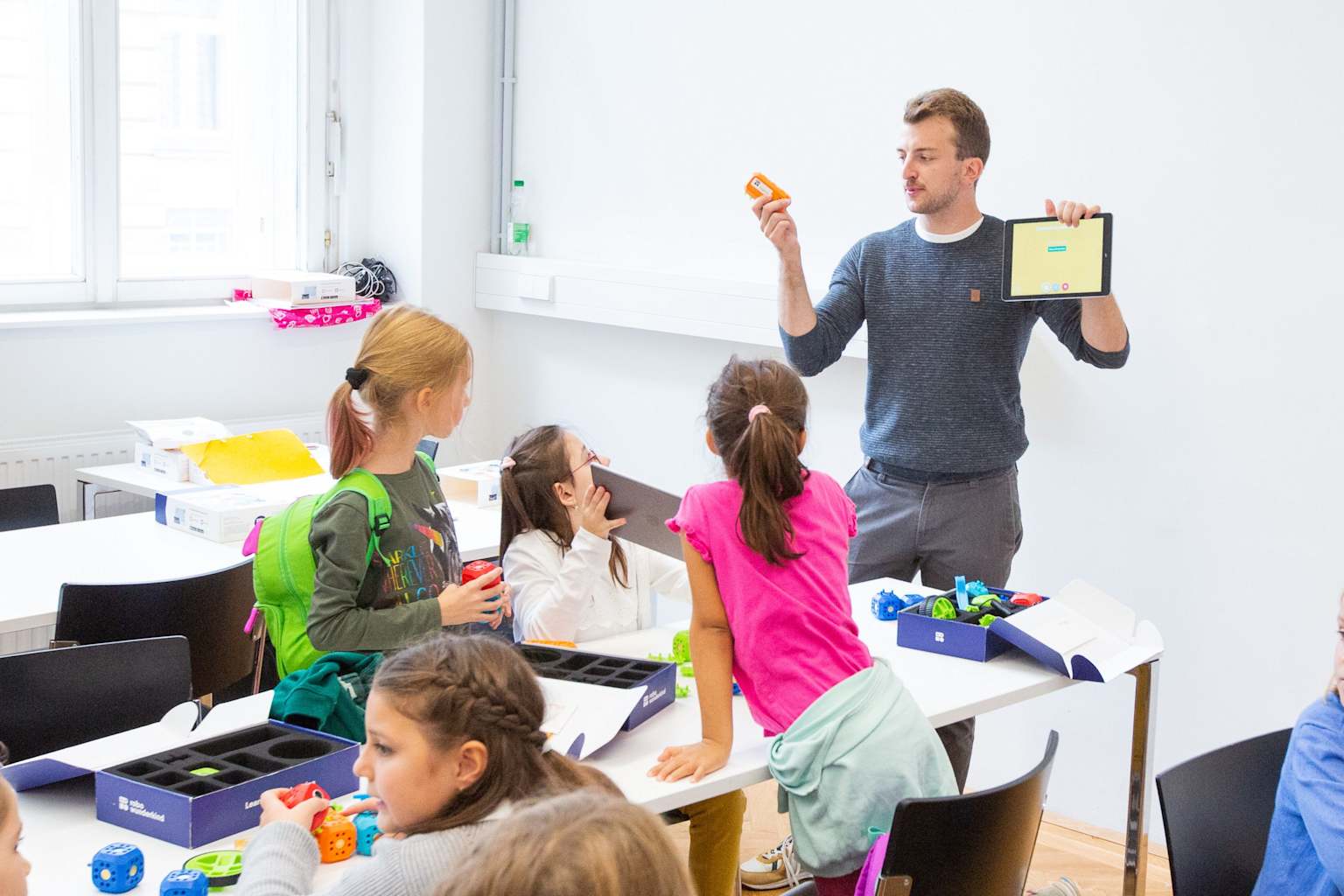 A male instructor guides young girls in a hands-on technology and robotics learning session.