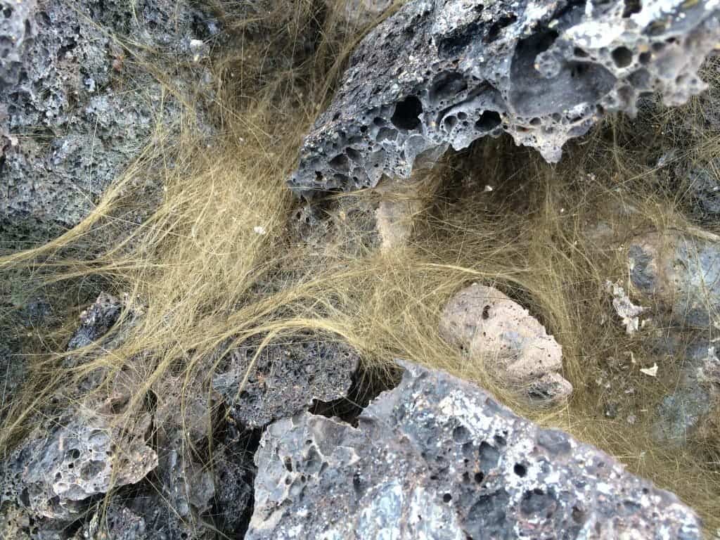 Fine strands of Pele's hair, a type of volcanic glass, are scattered among porous lava rock