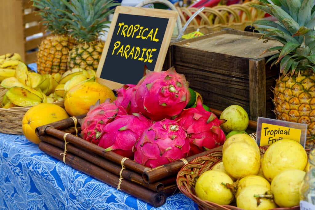 A colorful array of tropical fruits like dragon fruit, pineapples, and star fruit displayed at a Hawaiian farmer's market