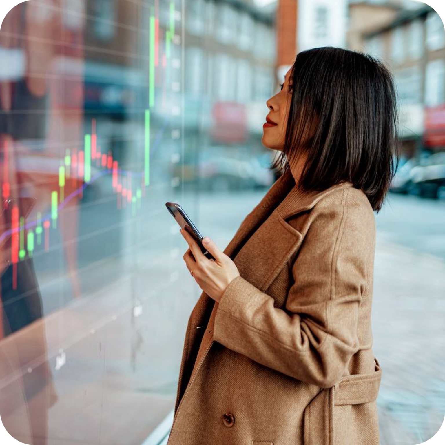 A person observes a digital stock market chart displayed on a transparent screen while holding a smartphone