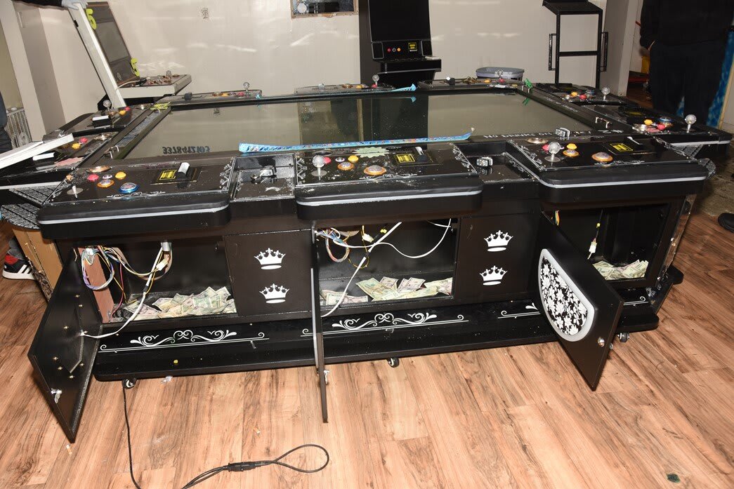 An illegal multi-player gambling machine with compartments open, revealing cash and exposed wiring, likely seized during a police raid